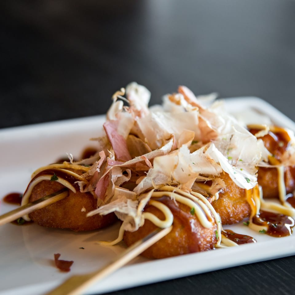 Takoyaki, a Japanese dish, with bonito flakes, mayonnaise, and sauce, served on a white plate.